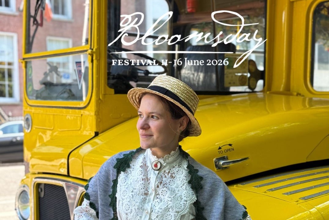 Bloomsday Afternoon Tea Trip, a smiling woman in Edwardian outfit with straw hat standing in front of a vintage yellow bus.