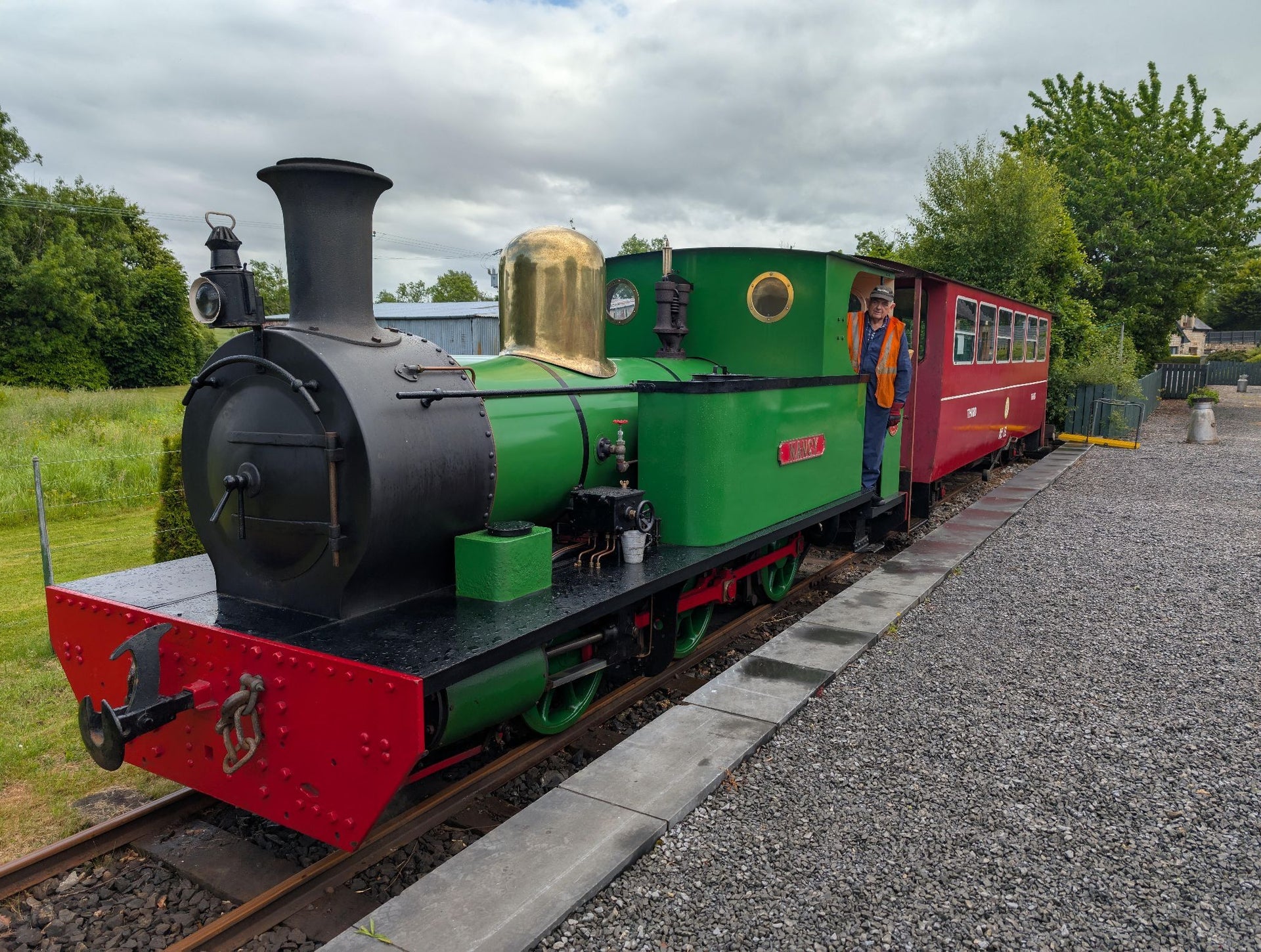 A small green steam engine at a platform pulling a single red passenger carriage