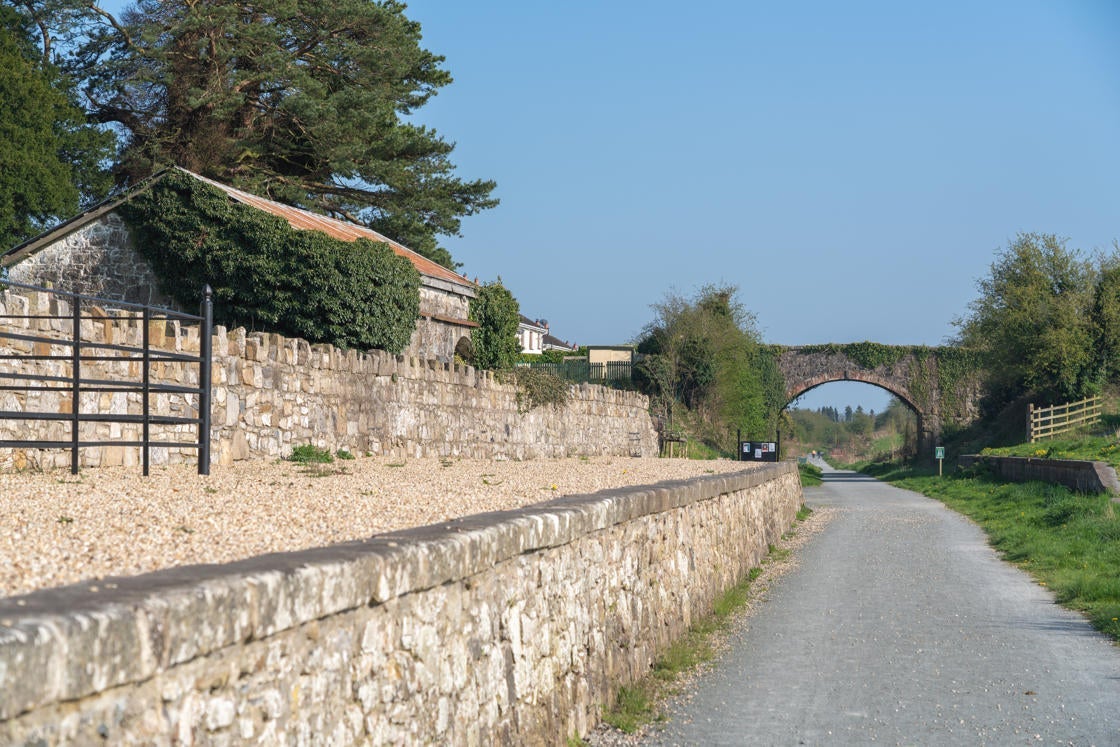 A walking path beside a stone wall continuing towards a stone bridge