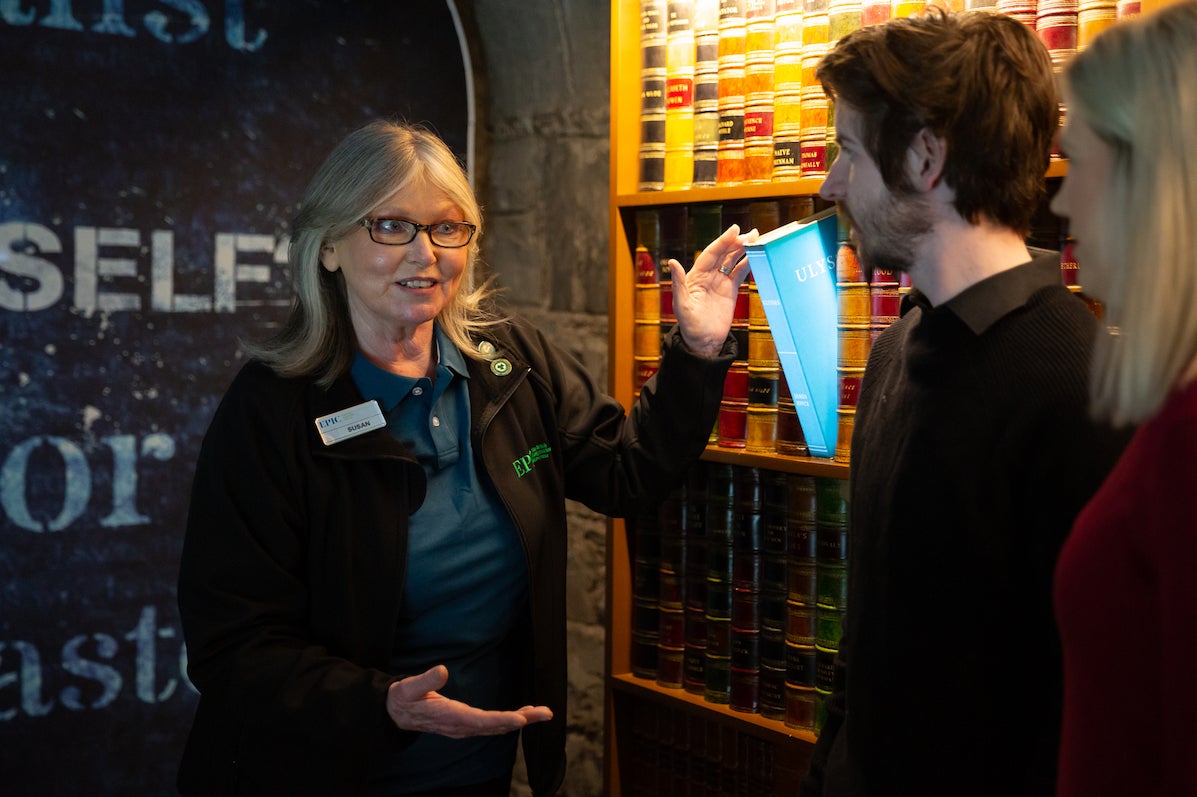 A tour guide is talking to 2 people beside an exhibit.