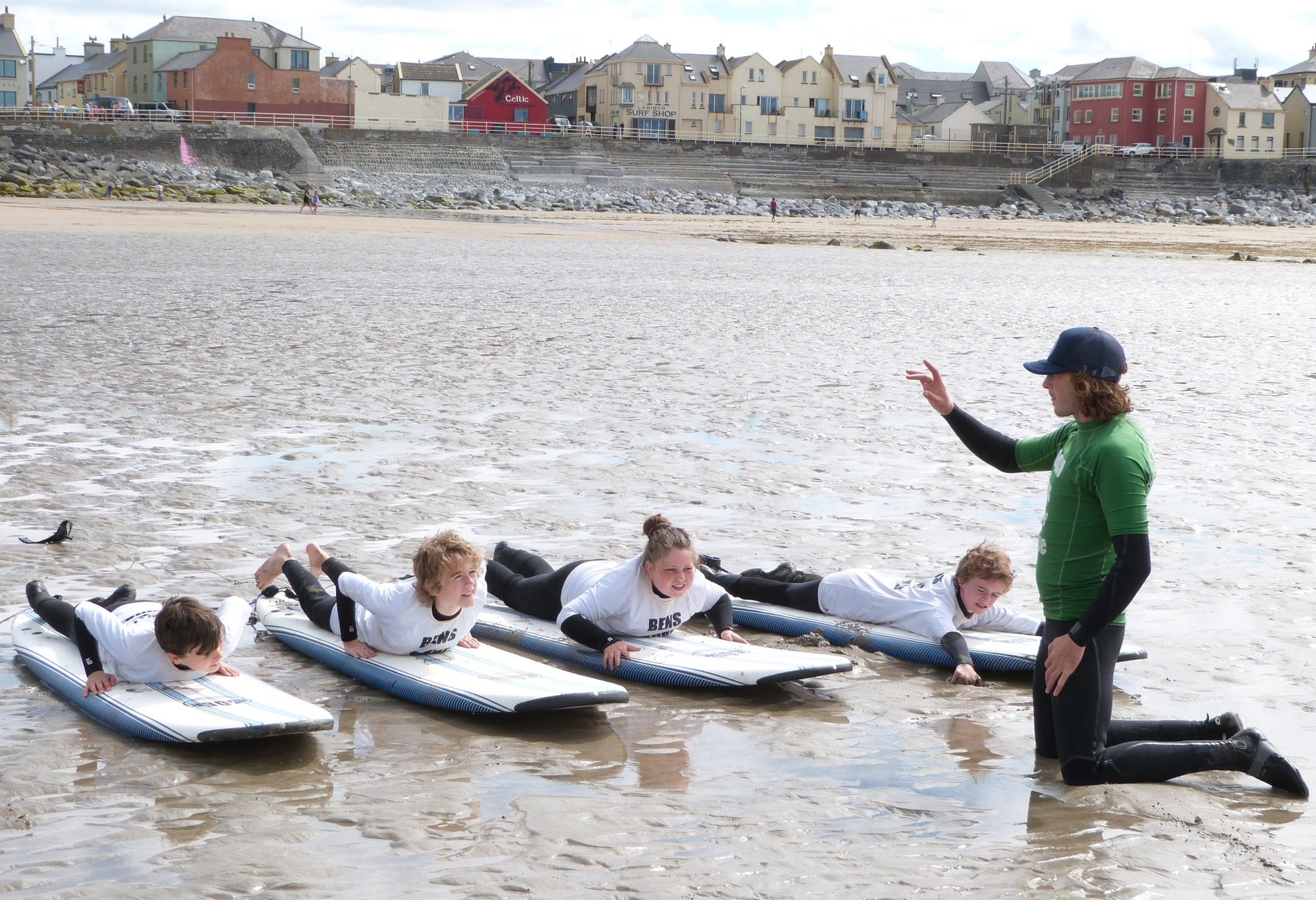 Four kids on surfboards on the stand with an instructor giving lessons