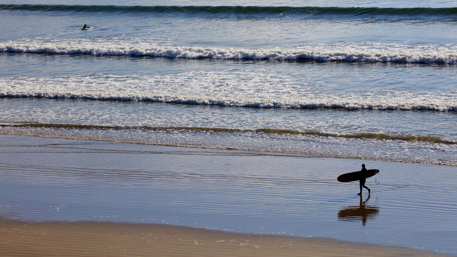 A surfer walks along the beach in Inch Stand, Dingle, Kerry