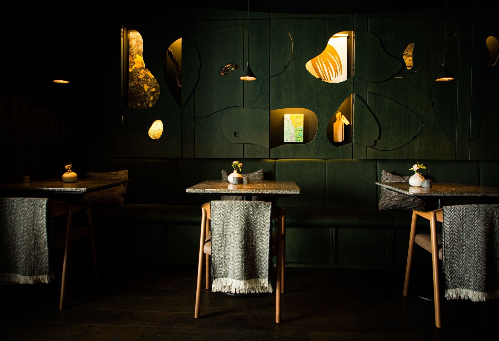 Three tables and chairs with grey scarfs on the back in a restaurant with dark green walls