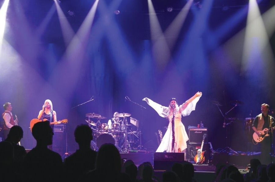 4 people on a stage playing musical instruments and singing.