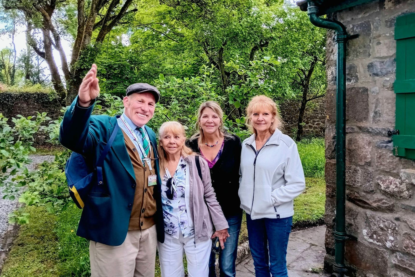 Three people standing with a tour guide next to a stone building with trees in the background