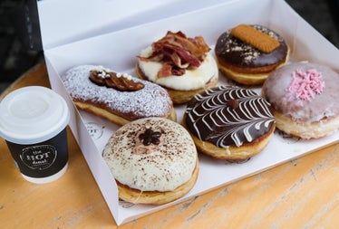 A box of colourful doughnuts on a counter beside a coffee cup