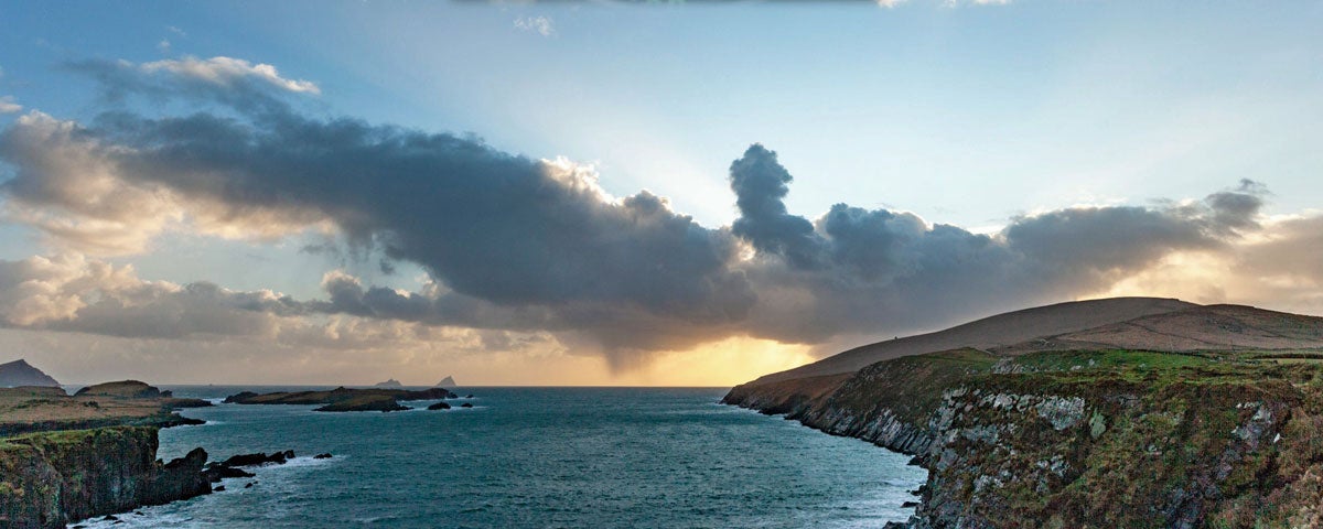 The Skellig Islands visible in the distance against a cloudy sunset taken from an inlet on the Skellig Ring coast