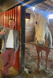 A man standing with a whiskey tasting glass beside a horse in a stable