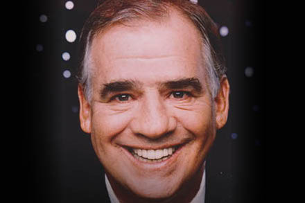Headshot of a smiling man with dark background.