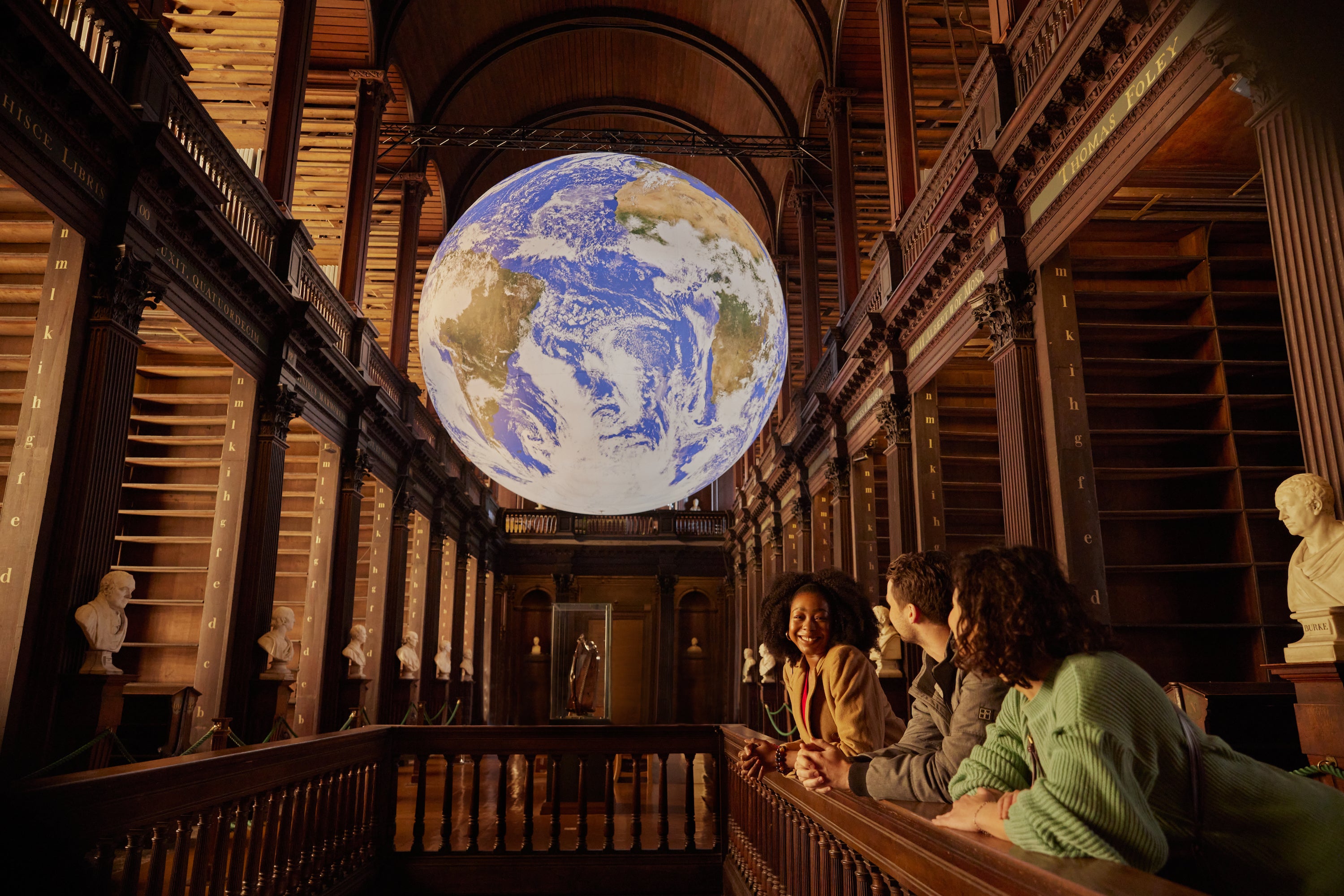 Gaia sculpture hanging above three people at Trinity's Old Library.