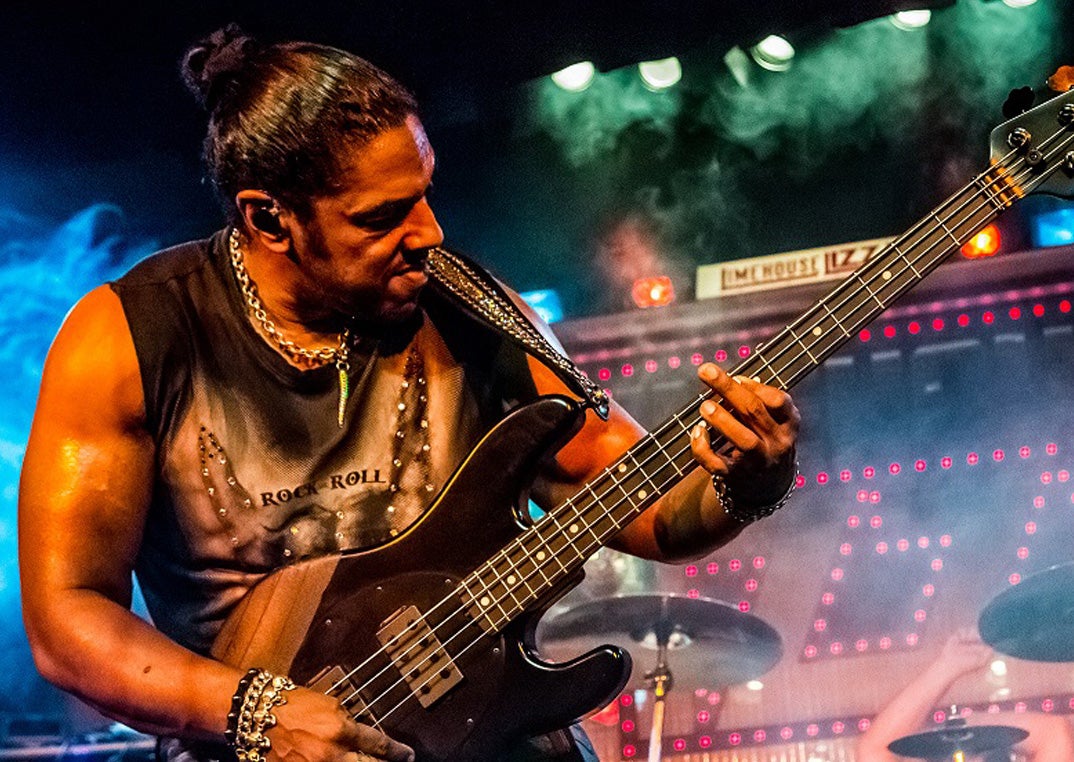 A man in leather trousers and gold jewelry is playing an electric guitar on a stage
