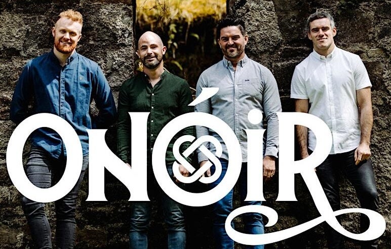 Contemporary Irish folk group Onóir, group of 4 smiling men standing in front of dark stone wall.