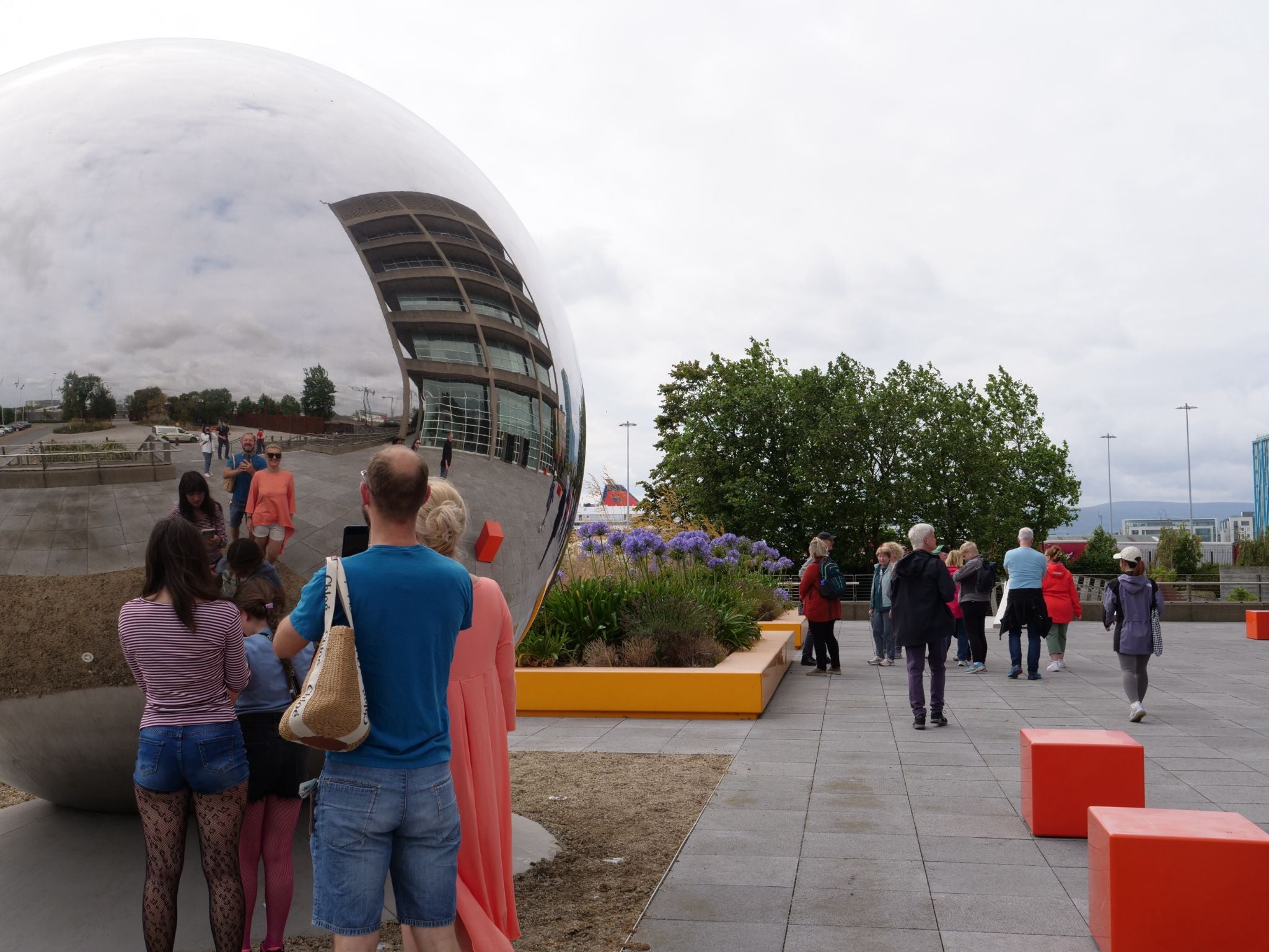 People looking at a large metal sphere in a city street
