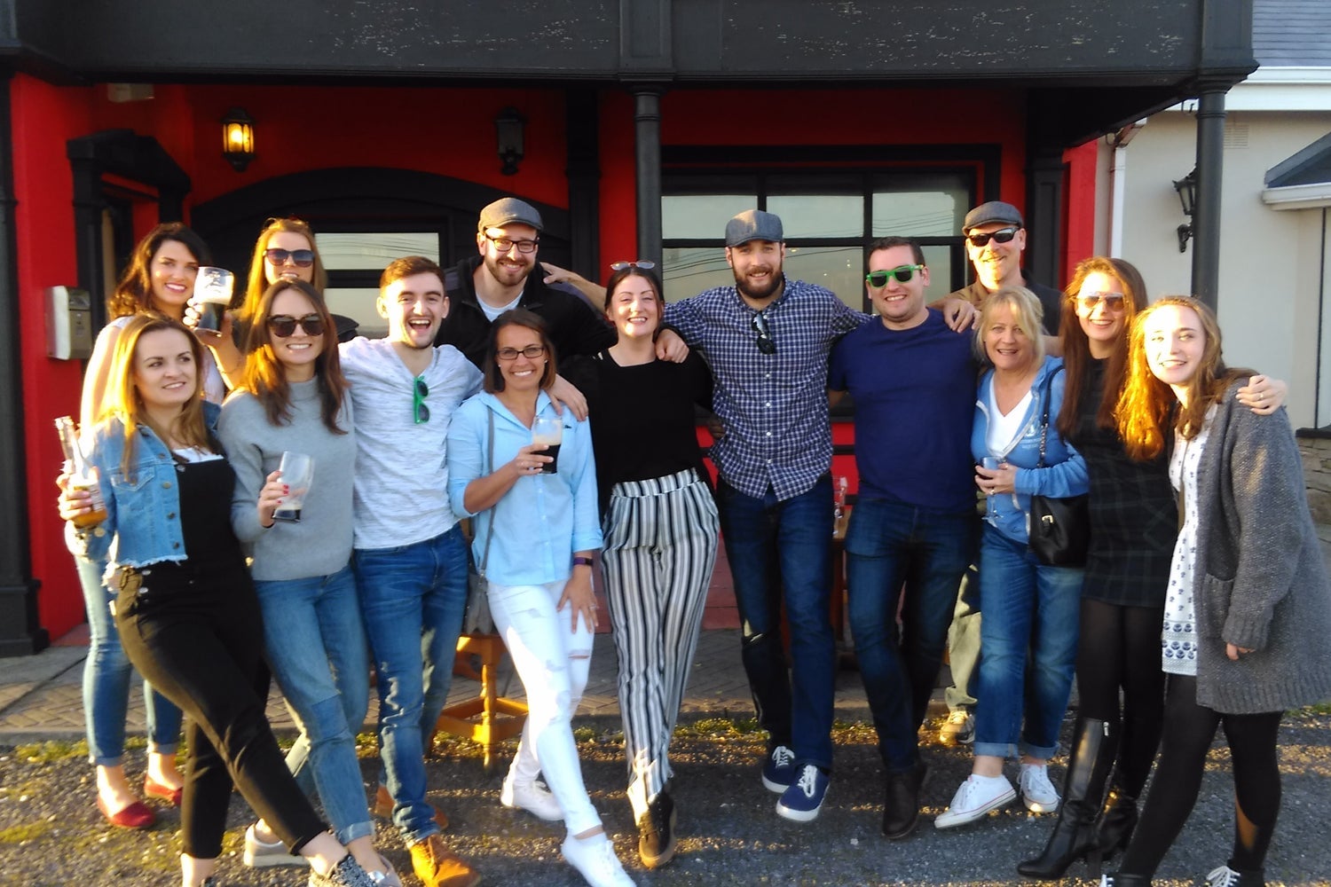 Group posing in front of a red and black building some holding drinks
