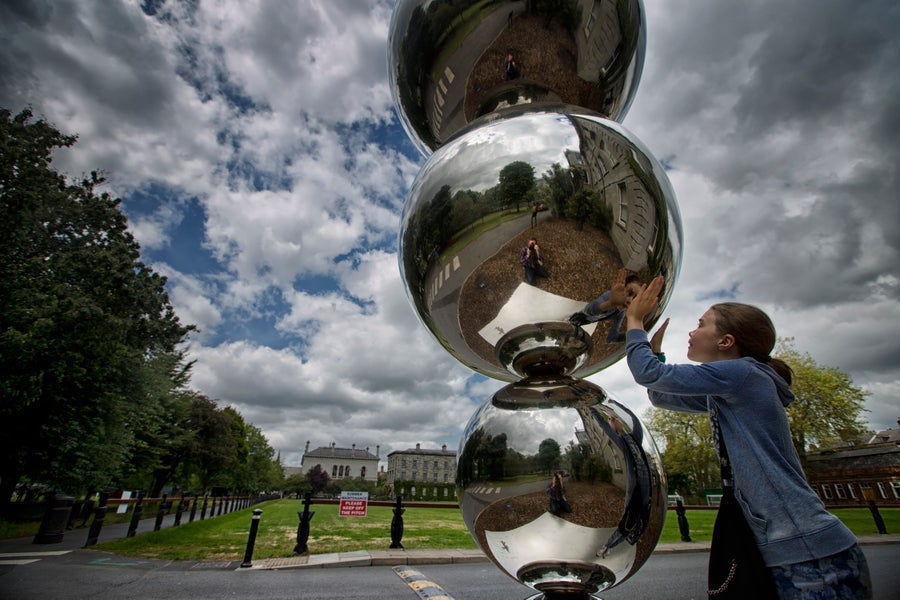 A girl looks at her reflection in the Atoms & Apples sculpture at Trinity College