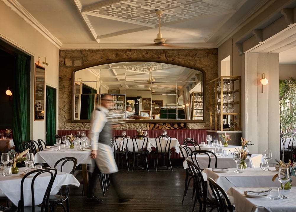 A member of staff walking through a dining room with a large mirror on the back wall