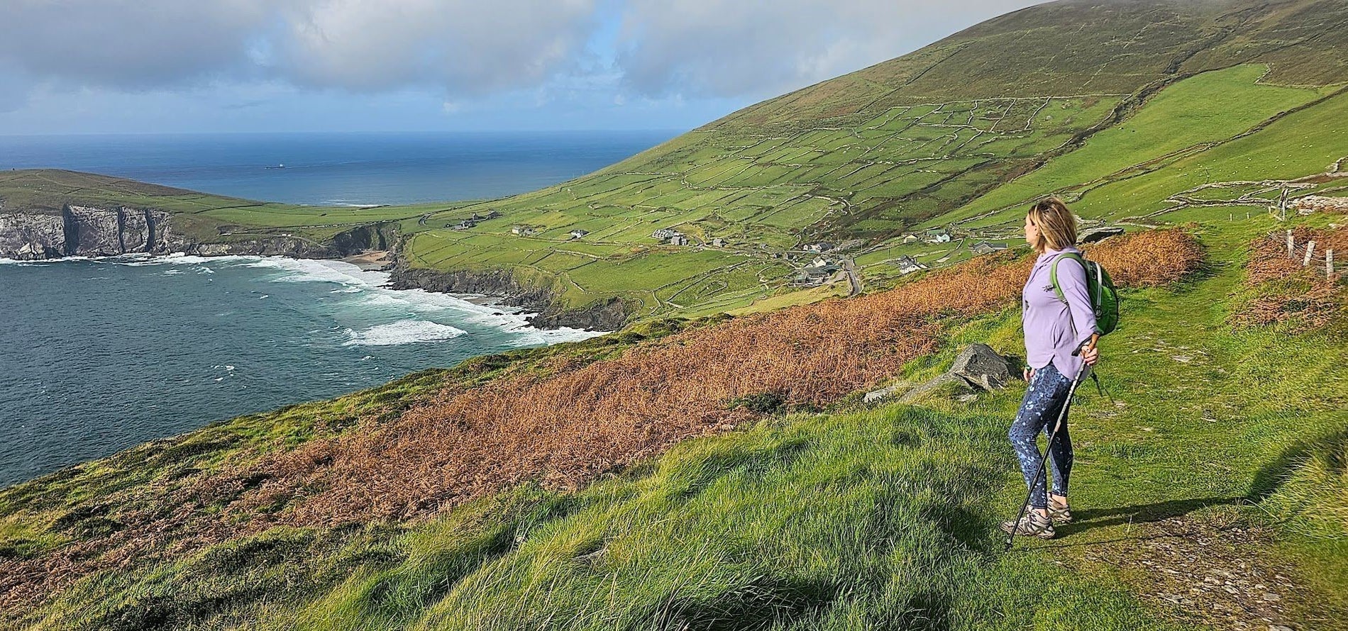 Person holding a walking pole standing in a field overlooking the sea