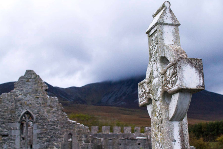 The ruins of an abbey in the background with a large high cross in the foreground.