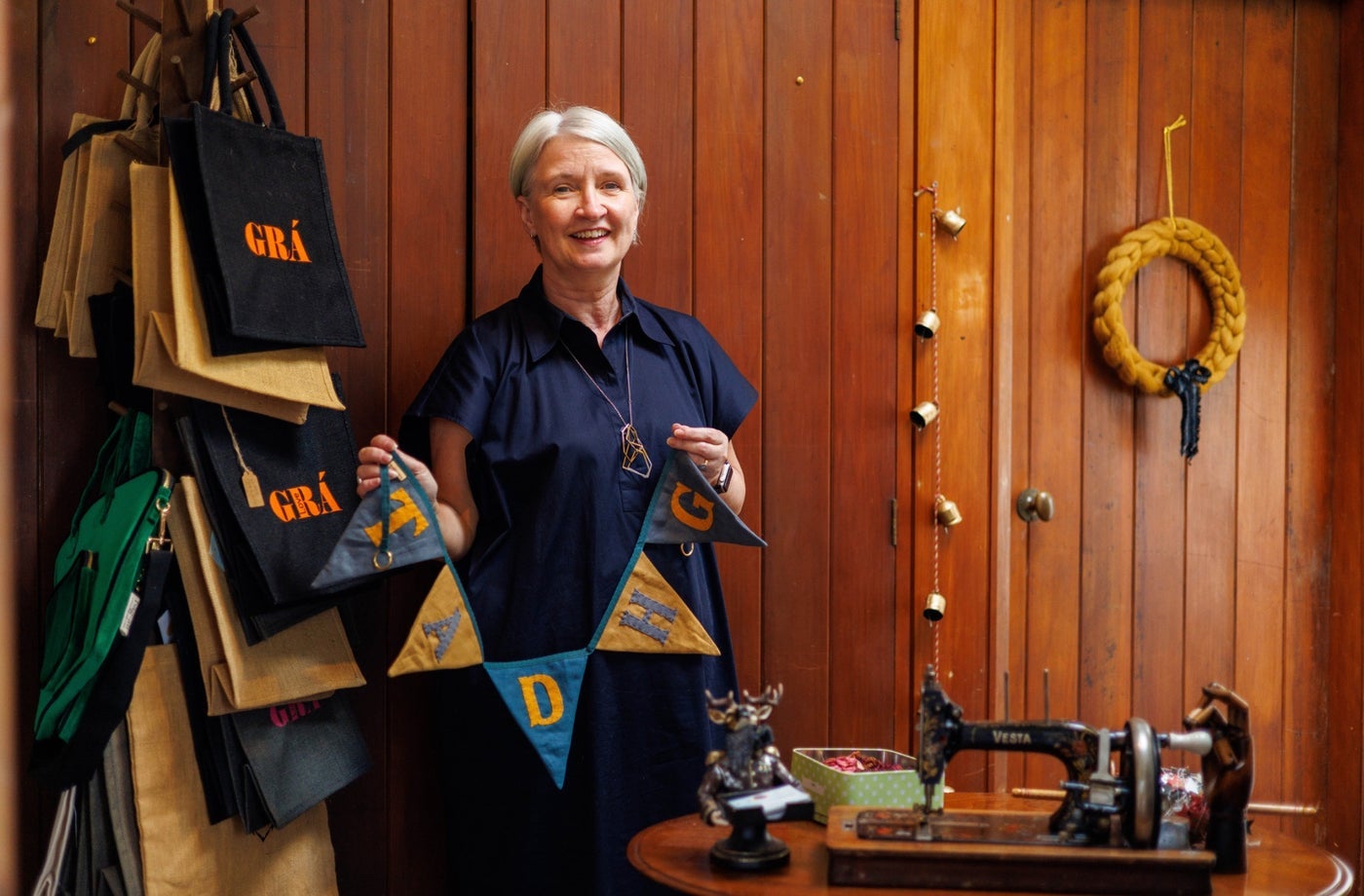 A lady standing in a workshop beside a sewing machine holding linen bunting