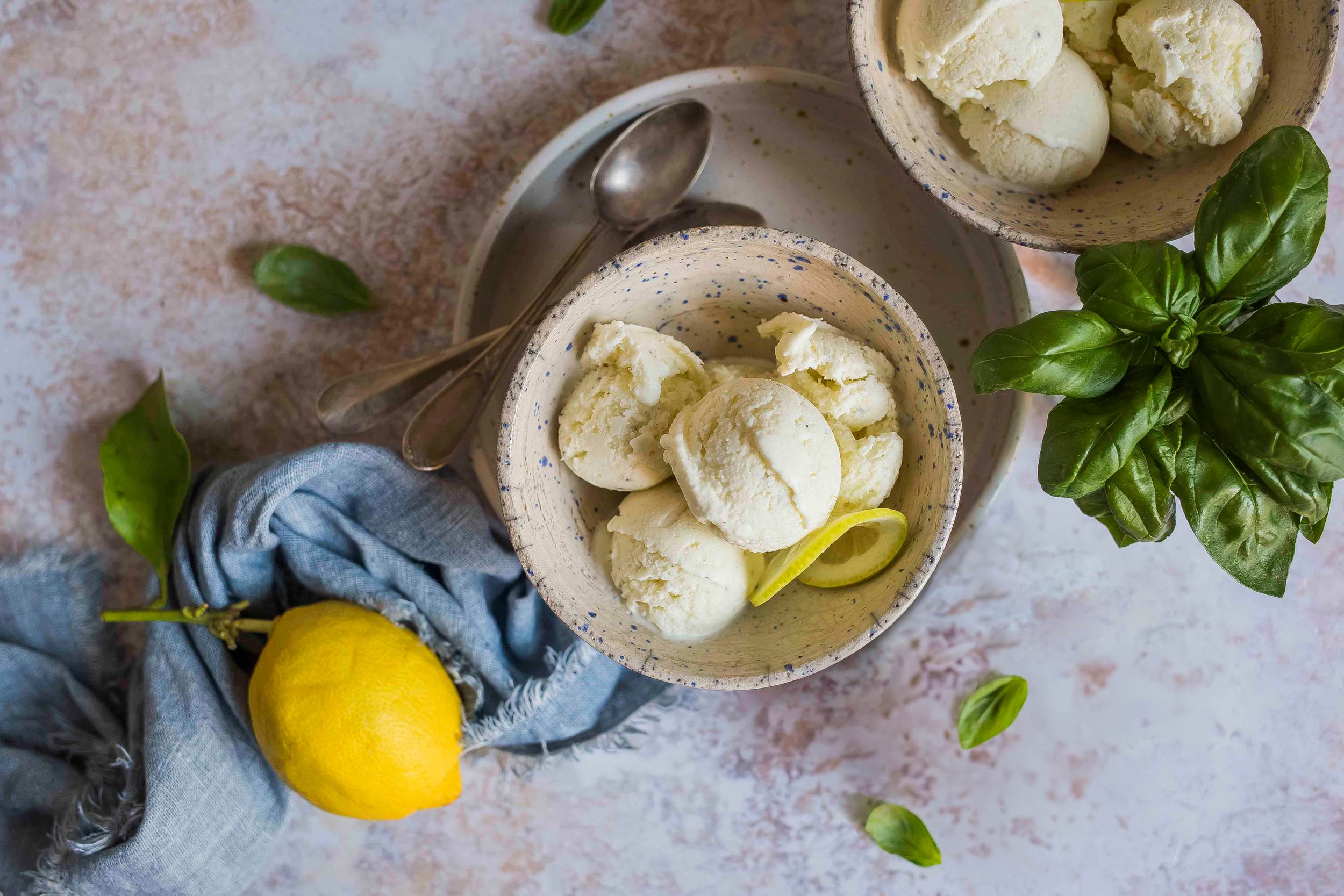 Gelato allo yogurt Latte Fieno servito in ciotola, decorato con scorza di limone e foglie di basilico fresche