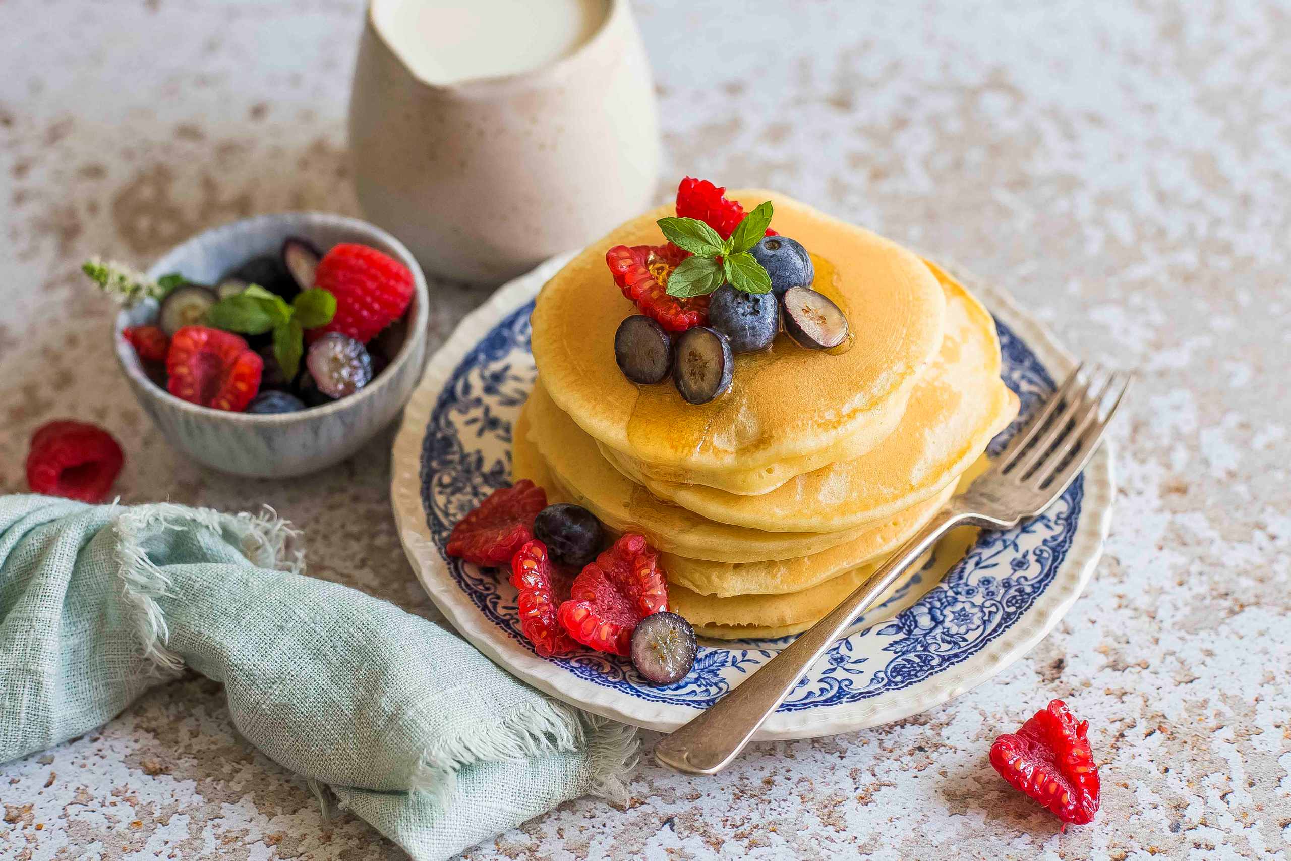 Fluffige Pfannkuchen mit frischen Beeren und Minzblättern auf einem verzierten Teller.