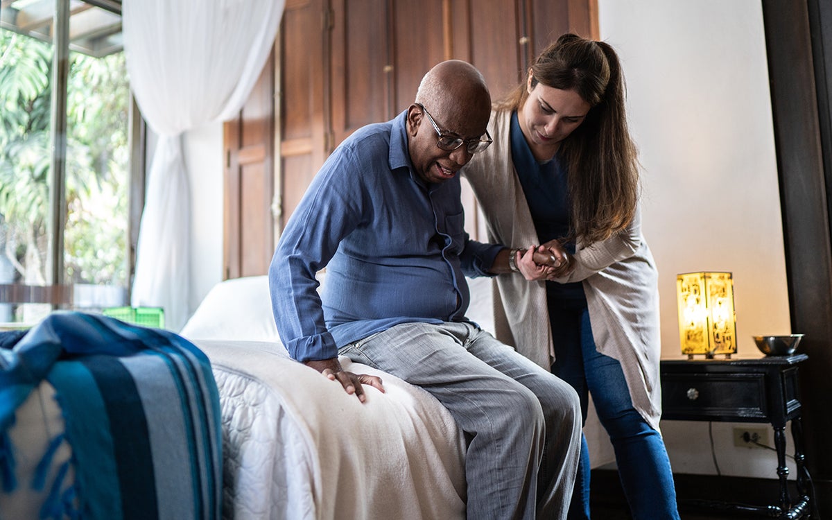 Een vrouw helpt een oudere man uit een bed.