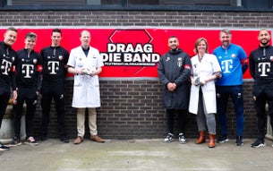 Voetballers van FC Utrecht en artsen van het UMC Utrecht staan voor een banner waarop 'Draag die Band' staat.