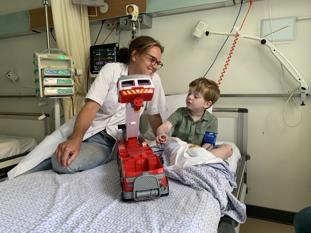 Een vrouw zittend op een bed naast een kind in een ziekenhuisbed