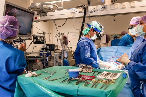 Vier chirurgen in de operatiekamer opereren een patiënt. Op de voorgrond staat een tafel met een groen kleed, vol met medisch gereedschap.