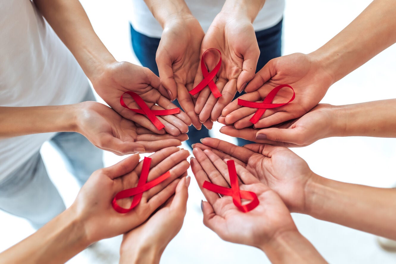 Diverse handen in een cirkel houden elk een rood lint vast, het symbool van HIV-bestrijding.