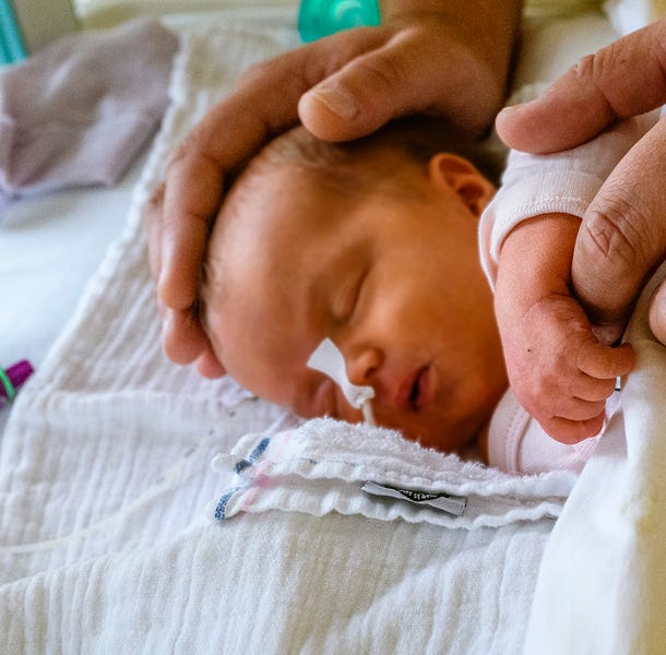 Verzorgende legt handen op een baby in een bedje