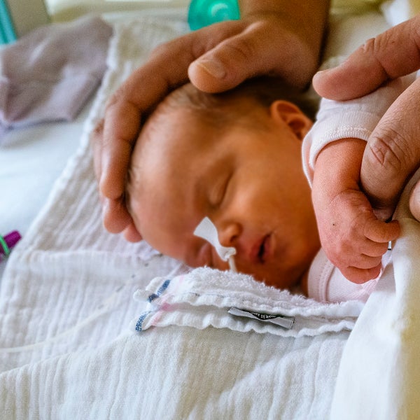 Verzorgende legt handen op een baby in een bedje