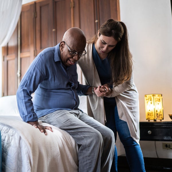 Een vrouw helpt een oudere man uit een bed.