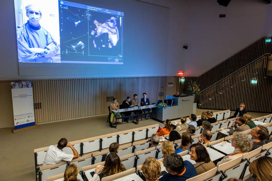 Bezoekers van het symposium zitten in een zaal en luisteren naar een presentatie