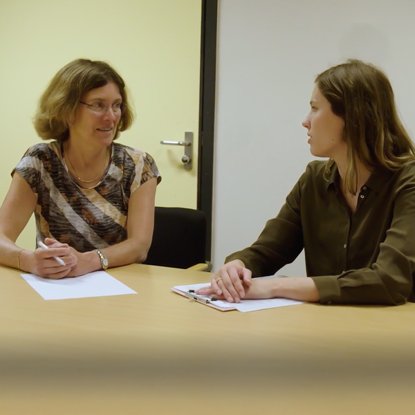 Een vrouw zittend aan een tafel met een vrouw die een pen vasthoudt in gesprek