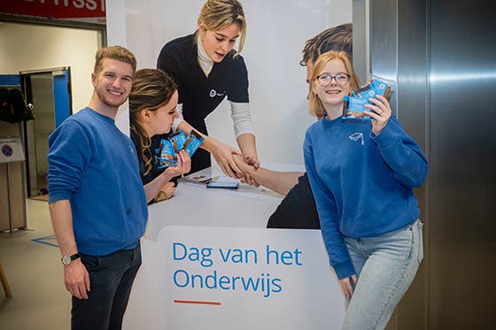 Vrolijke vrijwilligers delen materialen uit bij een registratiebalie tijdens de "Dag van het Onderwijs" evenement