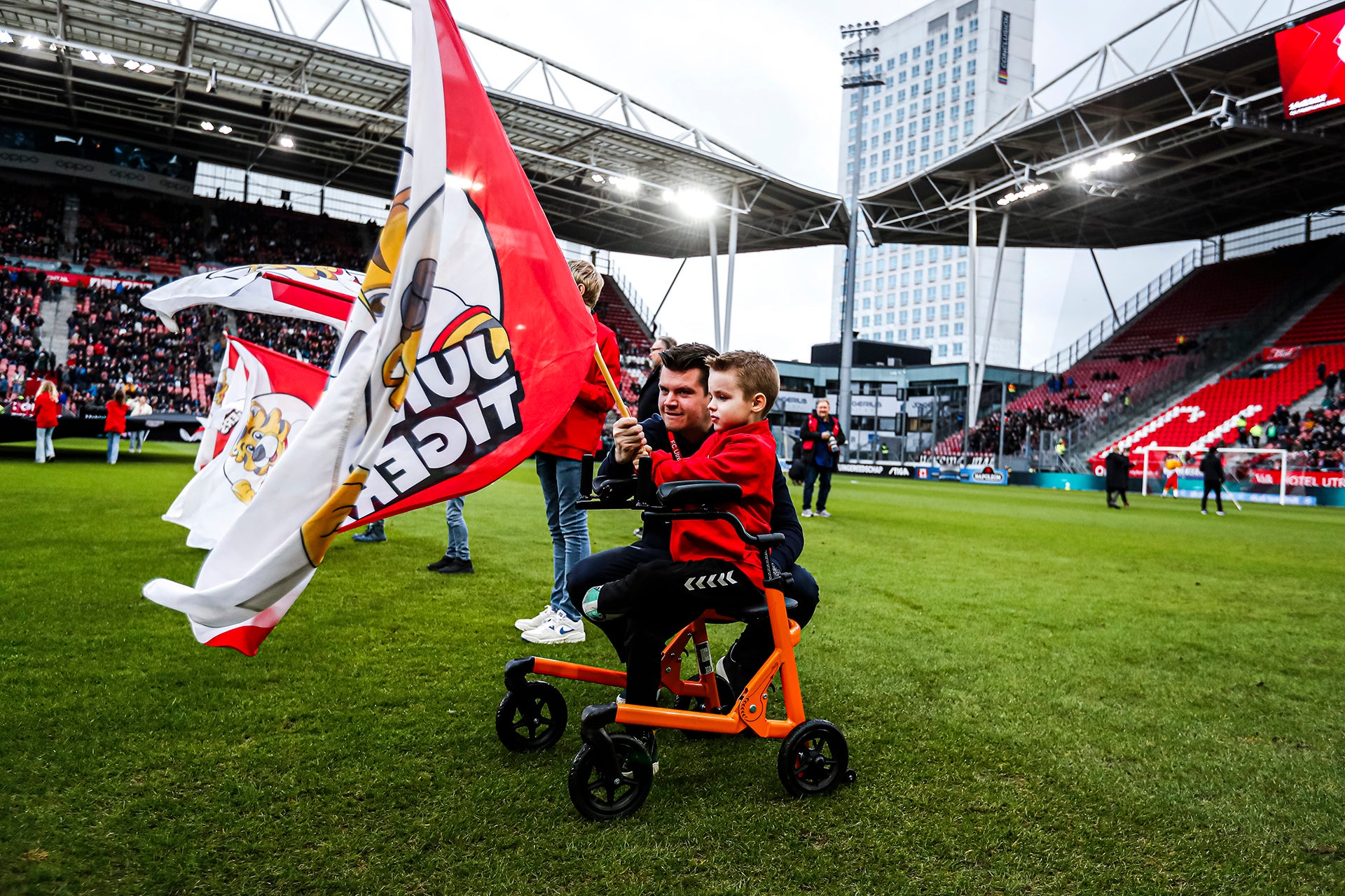 Een kleine jongen en zijn ouder/verzorger houden een FC Utrecht-vlag vast op het voetbalveld van Galgenwaard tijdens de WKZ-week van FC Utrecht.