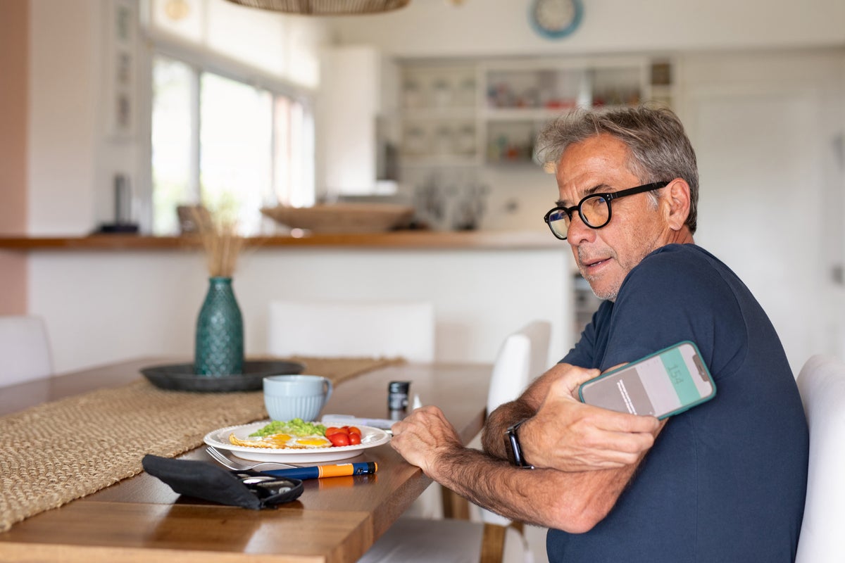 Een man aan een tafel met een bord eten meet zijn bloedsuikerspiegel met zijn telefoon