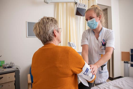 Een verpleegkundige met mondkapje houdt de arm van een patiënt vast