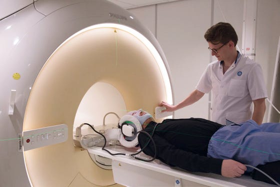 Een man met bestralingsmasker in een CT-scan. laborant staat ernaast