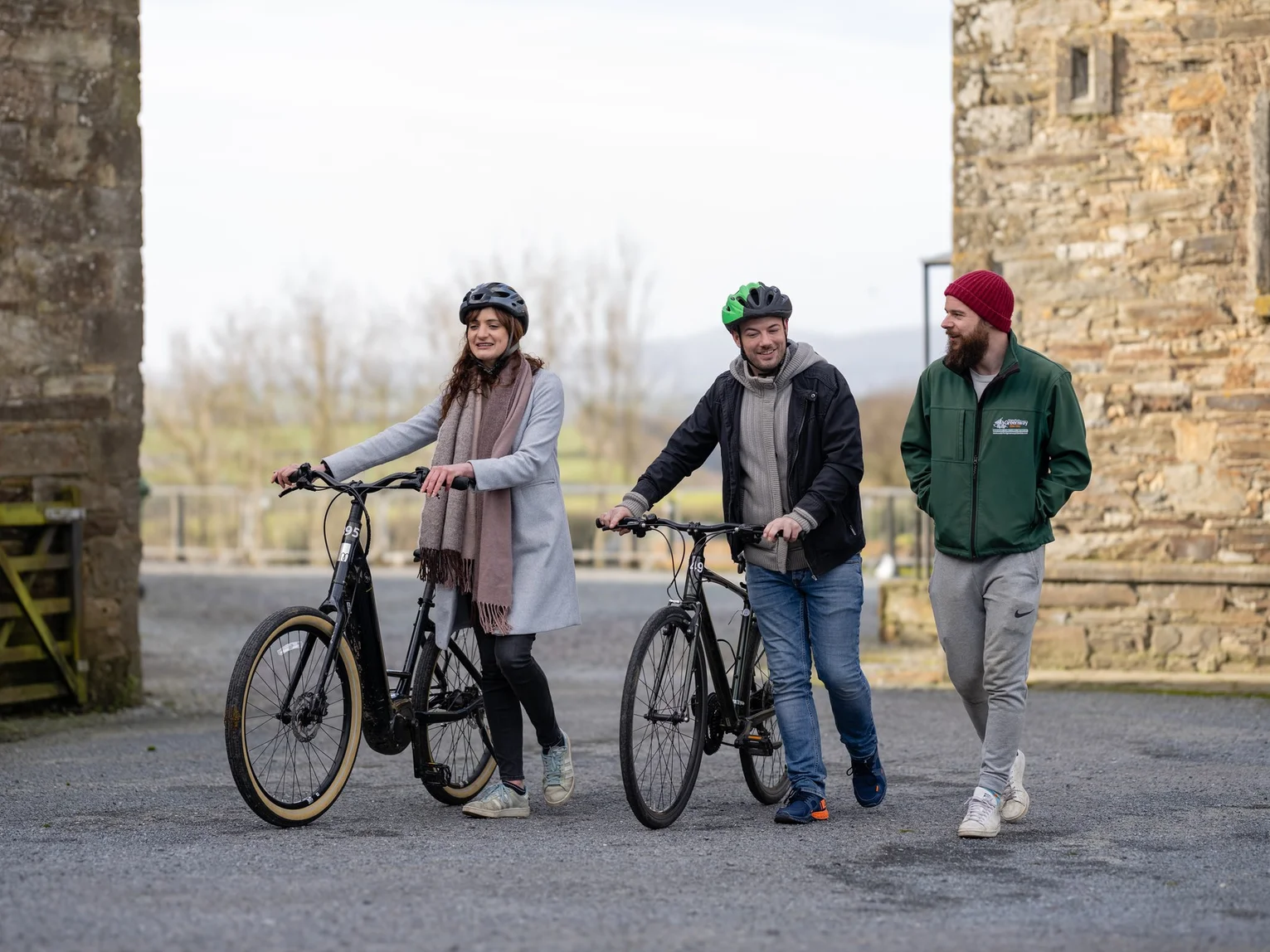 Three people walking with e-bikes outside a traditional stone building in the Irish countryside