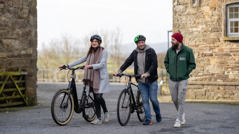 Three people walking with e-bikes outside a traditional stone building in the Irish countryside