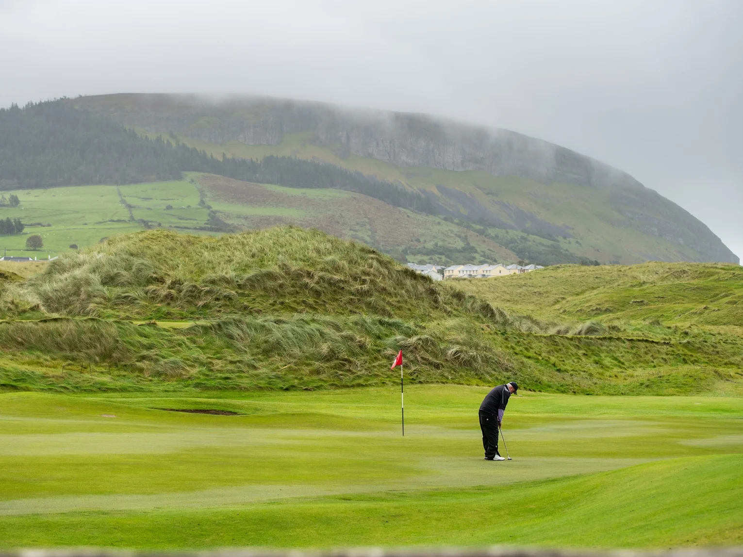 Lone golfer putting on a links green with misty hills and coastal scenery in the background