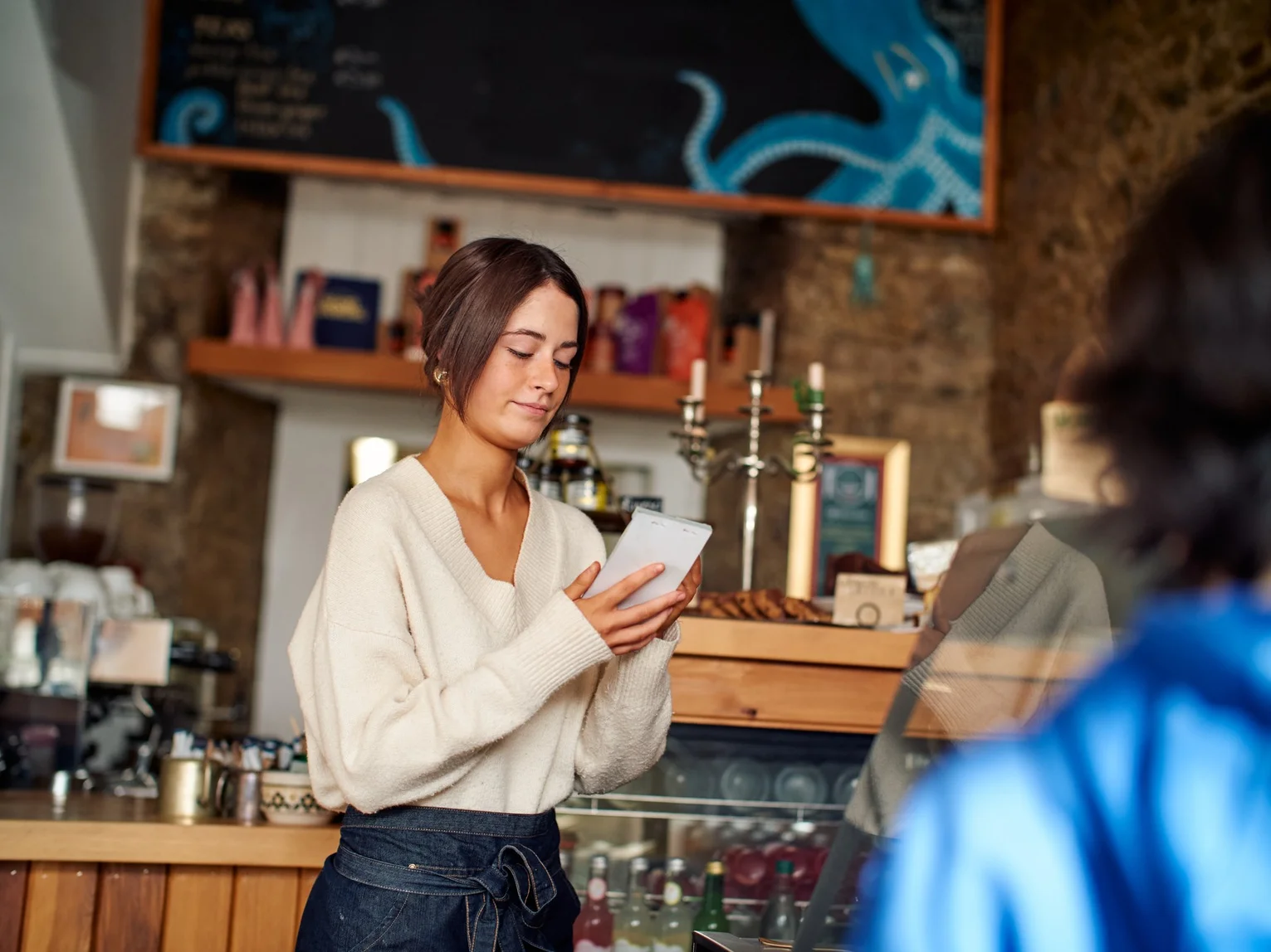 Café staff member writing in a notepad while serving a customer at a counter