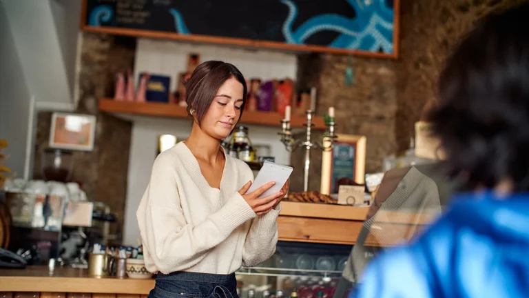 Café staff member writing in a notepad while serving a customer at a counter