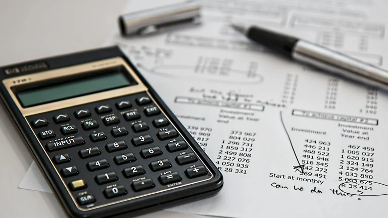 Financial calculator placed on printed investment spreadsheets with a pen