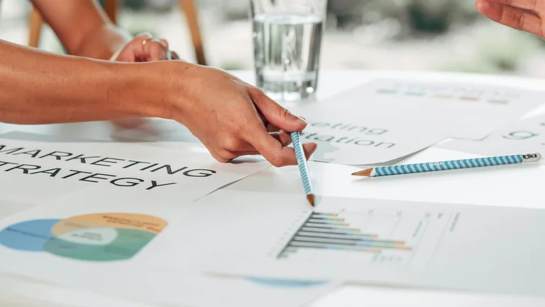 Two people reviewing marketing strategy documents and charts spread out on a table