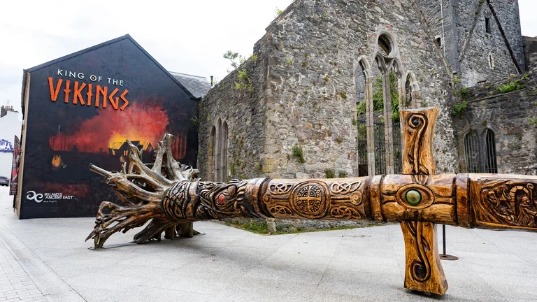 A large wooden sword in front of a stone building