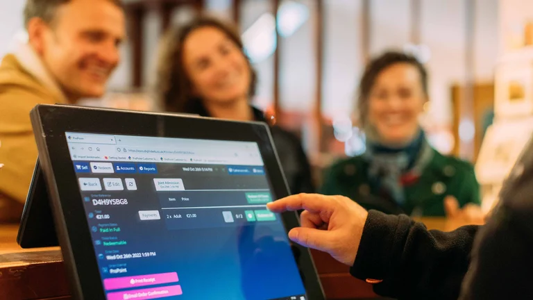 Staff member operating a touchscreen point-of-sale and ticketing system, with customers visible in the background