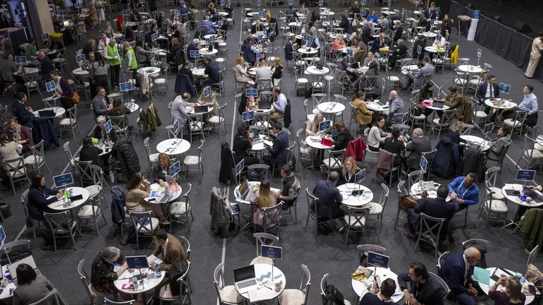 Overhead view of a large trade networking event hall with hundreds of attendees seated at round tables